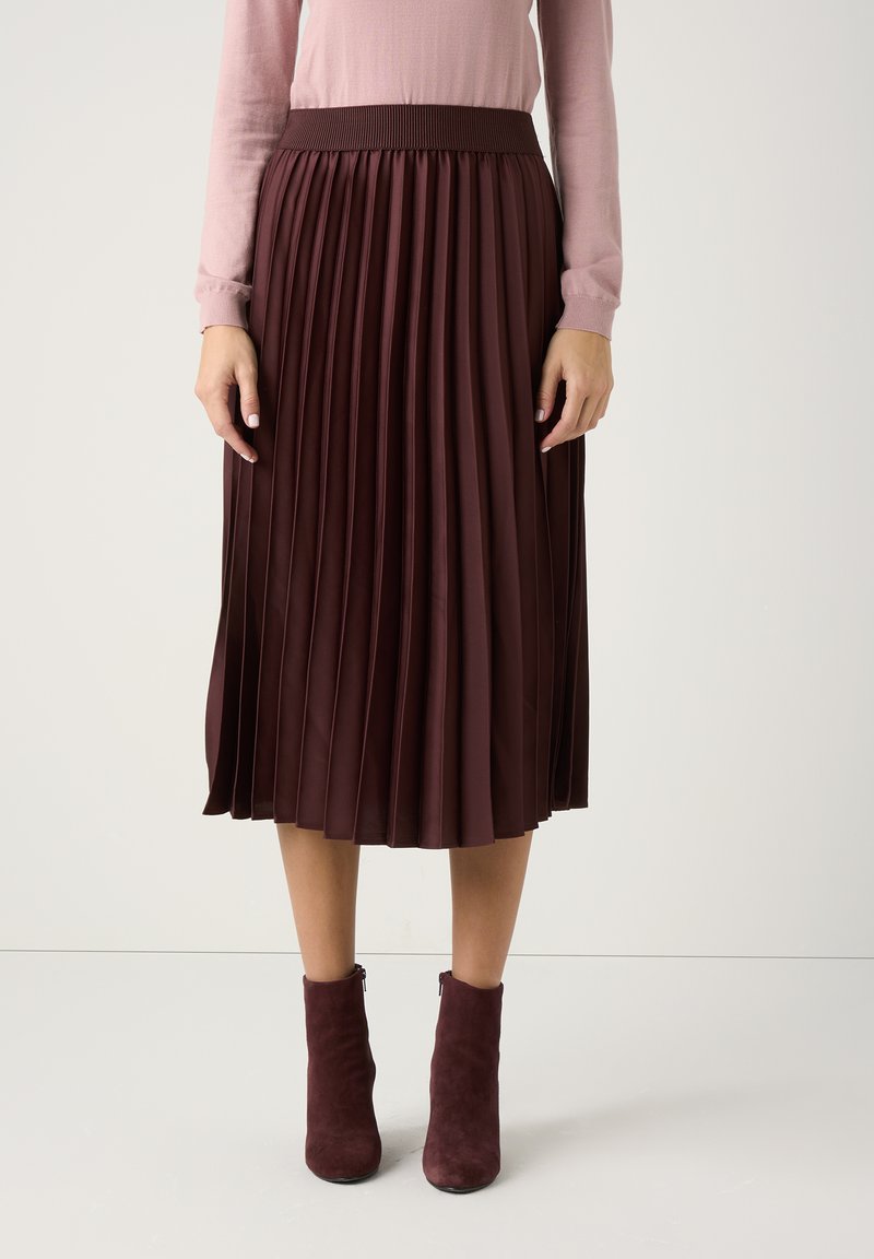 Burgundrote, plissierte Rock mit einem gerippten elastischen Bund, aus glattem Stoff, kombiniert mit burgundroten Knöchelstiefeln.