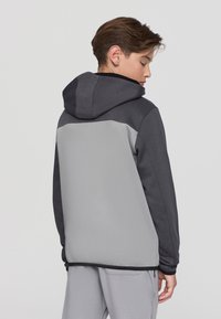 Felpa con cappuccio in materiali grigio scuro e grigio chiaro, caratterizzata da una superficie liscia e un design a blocchi di colore contrastanti sulla schiena.