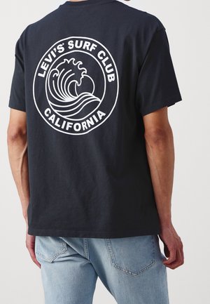 T-shirt en coton noir avec un graphique circulaire blanc représentant une vague et le texte "LEVI'S SURF CLUB CALIFORNIA" au dos.