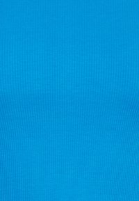 Hladká modrá tkanina s ribovanou strukturou. Tkanina vykazuje vertikální pruhy, vytvářející jemný vzor na povrchu.