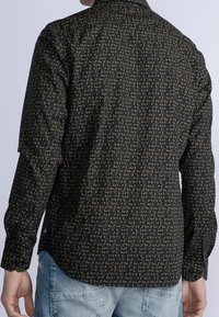 Camicia a maniche lunghe di colore blu scuro con un motivo geometrico dorato. Presenta un colletto e polsini abbottonati, realizzata in un tessuto leggero e liscio.