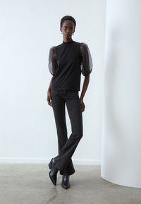 Top negru cu mâneci puff transparente, asortat cu blugi dark flared și cizme cu toc negre. Material neted cu un design ajustat.