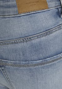 Uma calça de ganga azul clara com um deslizamento de couro visível rotulado "VERO MODA" na parte de trás. Apresenta detalhes de costura na frente e atrás.