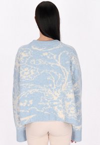 Pulover tricotat de culoare albastru deschis, cu un model floral crem. Are un guler rotund, mâneci lungi și o croială lejeră care se extinde până la șolduri.