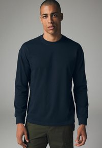 Dunkelblaues Langarm-T-Shirt aus Baumwolle mit Rundhalsausschnitt und gerippten Bündchen. Glatte Textur mit minimaler Ausstattung.