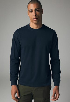 Donkerblauwe T-shirt met lange mouwen van katoen, met een ronde hals en geribbelde manchetten. Gladde textuur met minimale details.