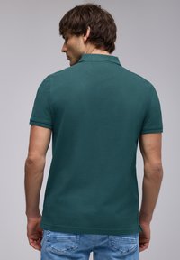 Grön polo skjorta med platt krage, korta ärmar och rak nederkant. Bärs med ljusblå jeans. Mjuk tygkvalitet med en slät textur.