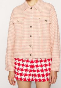 Růžový kabát s kostkovaným vzorem houndstooth s texturovaným povrchem, klasickým límečkem, zapínáním na knoflíky a dvěma náprsními kapsami.