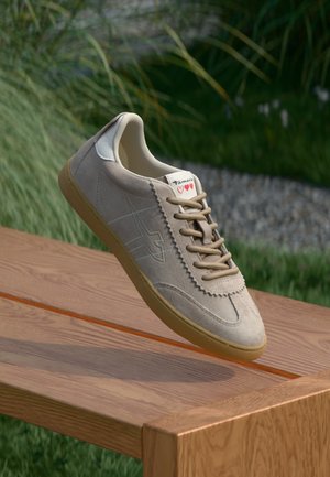 Beige suede sneaker with a smooth texture, rubber sole, and tan laces. Features a logo on the side and heart details on the label.