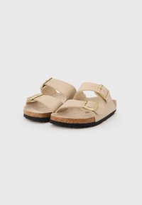 Μπεζ σανδάλια με δύο ρυθμιζόμενους ιμάντες, αγκράφες σε χρυσό τόνο, πάτο από φελλό και υφασμένο μαύρο λαστιχένιο πέλμα.