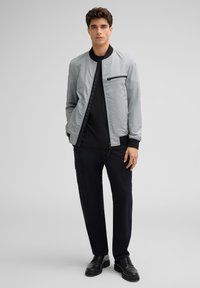 Grijze bomberjack met zwarte accenten, ritszak, gecombineerd met zwarte textuurbroek en zwarte schoenen. Glad materiaal, casual ontwerp.