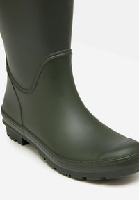 Zielony gumowy, wodoodporny but o gładkim wykończeniu, okrągłym nosku, niskiej podeszwie z bieżnikiem i subtelnym wykończeniu szwów w okolicy kostki dla większej elastyczności.