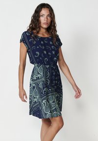Rochie bleumarin cu model paisley verde, cu mâneci scurte, talie elastică și fustă evazată; realizată dintr-un material ușor.