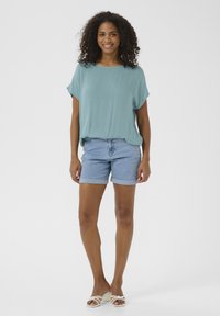 Himmelblaues, locker sitzendes Oberteil mit kurzen Ärmeln, kombiniert mit gerollten Denim-Shorts. Der Stoff wirkt weich und glatt. Einfaches, lässiges Design.