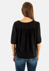 Blusa nera con texture e dettaglio arricciato sul retro, con maniche a palloncino corte, abbinata a jeans in denim blu.