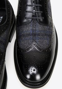 Zwart lederen en grijs wollen brogue schoenen met een ruitpatroon, decoratieve perforaties en een glanzende neus. Klassiek wingtip ontwerp.