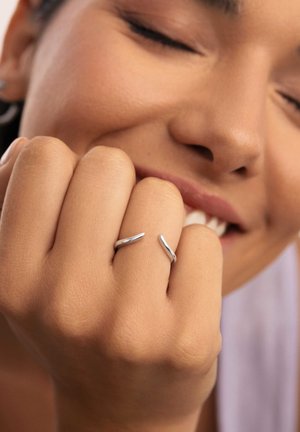 Anillos de plata con un diseño liso y curvado, reposando parcialmente sobre una mano. La mano tiene una textura ligera, con los dedos suavemente curvados.