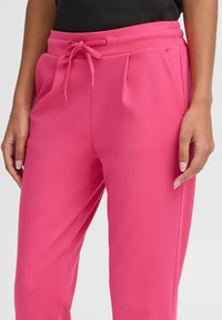 Rosa Sweatpants mit einem elastischen Bund und Kordelzug, Falten an der Vorderseite und einer glatten, weichen Textur.