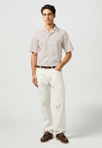 Camicia a maniche corte, di un rosa chiaro a fantasia con colletto bianco, abbinata a pantaloni bianchi e scarpe marroni con lacci rosa. Stile semplice e vestibilità rilassata.