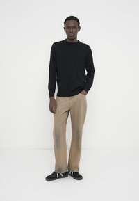 Haut noir à manches longues en tricot associé à un pantalon marron clair légèrement délavé et des baskets noires avec des accents blancs. Design simple et épuré.
