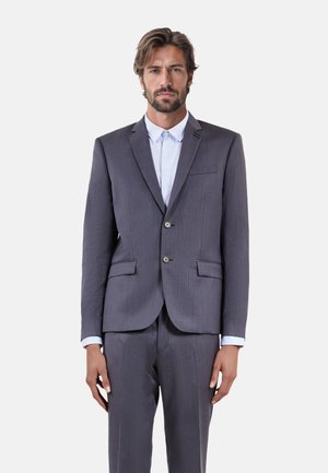 Abito grigio a righe sottili con una vestibilità su misura, due tasche frontali e bottoni argentati. Sotto, una camicia azzurro chiaro con colletto a punte.
