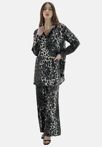 Ensemble deux pièces à imprimé léopard en tissu soyeux ; comprend une chemise ample à boutons et un pantalon large en tons noirs et crème.