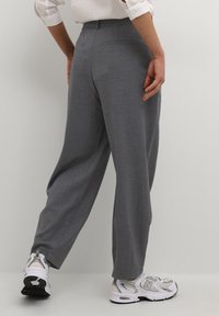 Pantalon gris sur mesure à coupe droite, doté de deux poches arrière et d'une texture lisse. Associé à des chaussures de sport blanches et grises.