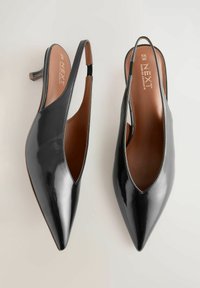 Schwarz lackierte Slingback-Absatzschuhe mit spitzer Zehe, offenen Seiten und einer braunen Lederinnensohle. Mittelhoher Stiletto-Absatz.