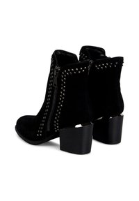 Botines de ante negro con tachuelas metálicas en las cremalleras, un tacón cuadrado y una textura suave, que muestran un diseño contemporáneo.