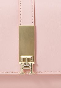 Pink leather handbag featuring a gold-tone hardware clasp with a geometric design. Smooth texture with stitched detailing along the edges.