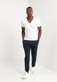White V-neck t-shirt paired with navy jogger pants and white sneakers, featuring a fitted design and soft fabric texture.