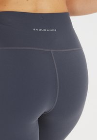 Korkeavyötäröiset tummansiniset legginsit, jotka on valmistettu joustavasta kankaasta. Niissä on litteät saumat ja vyötäröllä "ENDURANCE" -logo.
