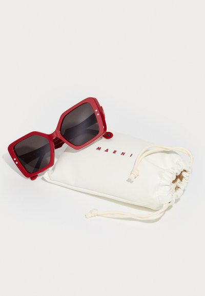 Occhiali da sole rossi in plastica con grandi montature quadrate e lenti scure, accompagnati da un sacchetto bianco con coulisse che riporta la scritta "MARNI" in rosso.
