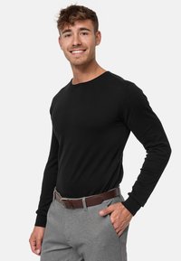 Svart langermet skjorte med rund hals, kombinert med lysegrå bukser og et brunt belte. Jevn tekstur, tettsittende design.