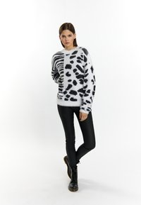 Flauschiger weißer Pullover mit schwarzem Tiermuster und Streifen, kombiniert mit schwarzen Lederhosen und schwarzen Schnürstiefeln.