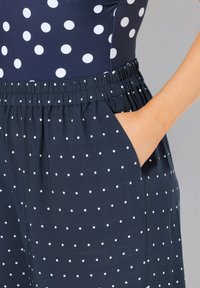 Marineblauwe stof met witte stippen; beschikt over een elastische tailleband en zakken; gladde textuur en ontwerp met een losse pasvorm.