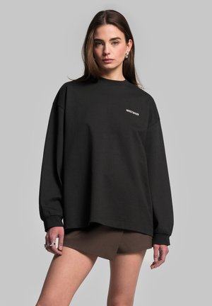 Czarny, oversize sweatshirt z ribbami przy mankietach i okrągłym dekoltem. Na lewej stronie znajduje się logo "WRSTBHVR" w białym kolorze. Materiał z teksturowanej bawełny.