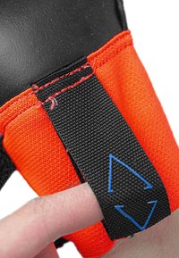 Black and orange glove with textured grip, featuring a black strap with blue arrows for adjustment and red stitching along the seams.