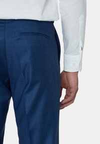 Marineblauwe op maat gemaakte broeken met een gestructureerde afwerking, voorzien van een achterzak en gecombineerd met een wit overhemd met knopen. Hand gepositioneerd op de taille.