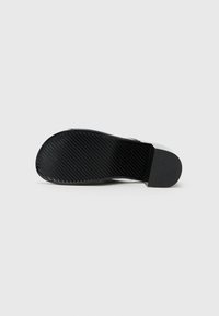 Sola de sapato preta com um padrão texturizado, feita de material de borracha e com um salto ligeiramente elevado. Bordas suaves e forma curva.