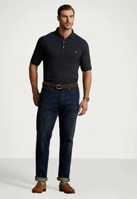 Σκούρο μπλε πόλο μπλούζα με κοντά μανίκια, συνδυασμένη με σκούρες τζιν παντελόνες, καφέ δερμάτινη ζώνη και αντίστοιχα παπούτσια. Καθαρή, κλασική εμφάνιση.