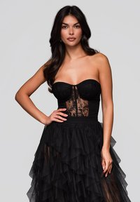 Svart strapless klänning med en spets överdel och ett lager av tyllkjol, med en figurnära midja och en volang i nederkanten. Elegant och texturerad design.