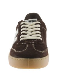 Zapatillas de ante marrón con acentos en blanco, parte delantera con cordones, puntera redonda y suela de goma. Presenta costuras visibles y una etiqueta en la lengua.