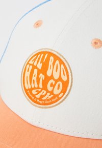 Gorra de béisbol con una corona blanca, visera naranja y un parche redondo de logo naranja. Presenta costuras azules y una tela texturizada.