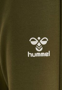 Olijfgroene kleding met een gladde textuur, voorzien van een wit "hummel" logo en embleem, geplaatst in de onderste hoek.
