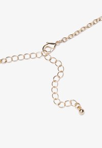 Gouden metalen ketting met ovale schakels, voorzien van een karabin slot en een hanger met een kraal aan het einde. Glad oppervlak en uniforme kleur.