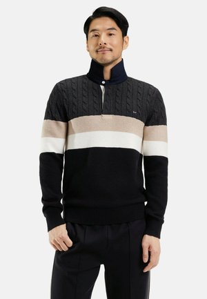Pull coloré en noir, beige et blanc. Texture en tricot côtelé avec un col zippé mi-hauteur. Ourlet et poignets côtelés, avec un logo subtil.