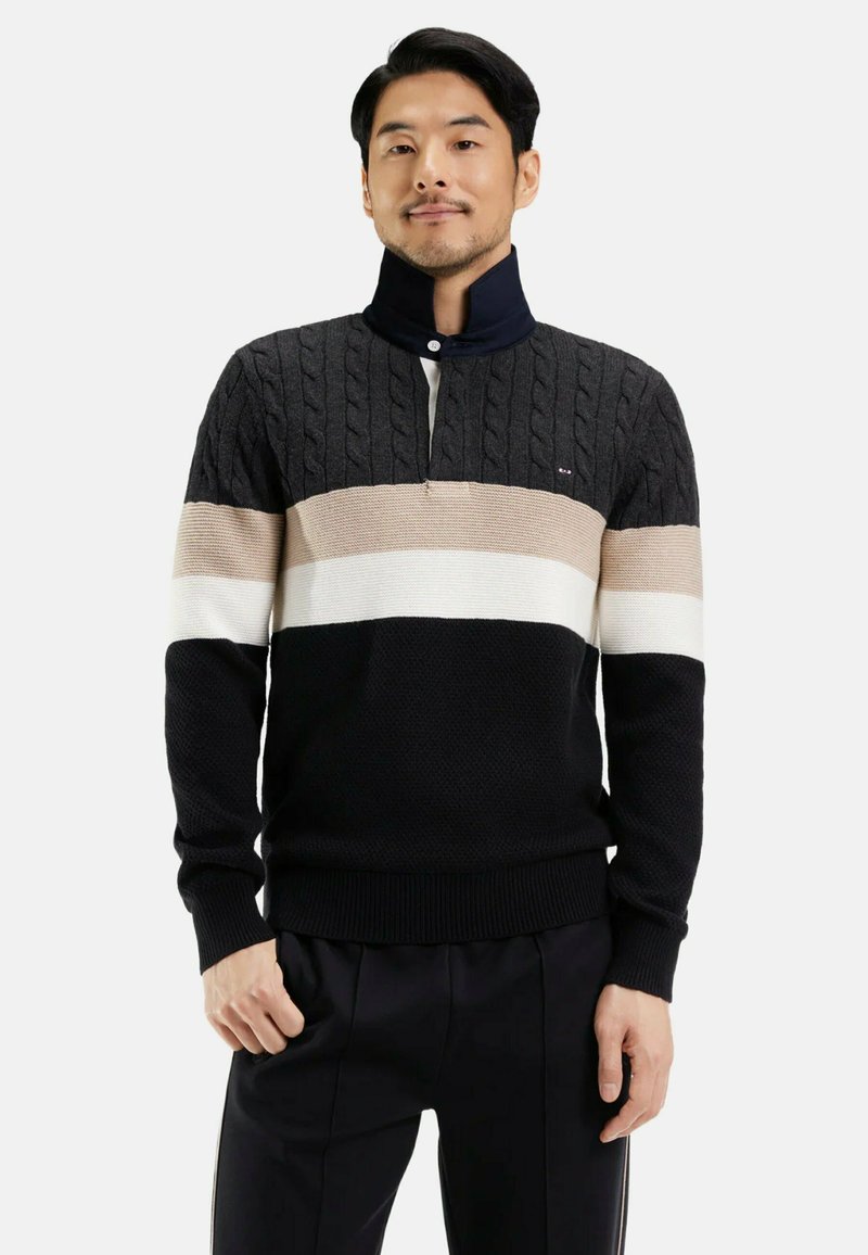 Pull coloré en noir, beige et blanc. Texture en tricot côtelé avec un col zippé mi-hauteur. Ourlet et poignets côtelés, avec un logo subtil.