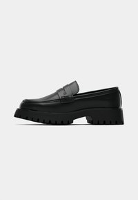 Black leather loafers with a textured strap and thick, ridged sole. Smooth upper with detailed stitching along the edges.