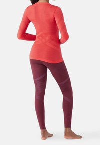 Maglietta rossa aderente a maniche lunghe abbinata a leggins bordeaux scuro. La maglietta presenta un design testurizzato, mentre i leggins hanno motivi geometrici.